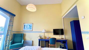 Ett hotellrum med en säng, ett skrivbord med en stol, en tv och ett fönster med gardiner.