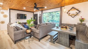 A modern living room with a grey sofa, a small table, and a dining area with a wooden table and chairs.