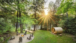 A forested outdoor area with a fire pit, seating, and a cylindrical structure.