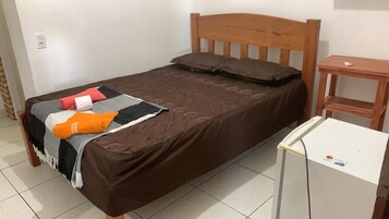 Uma cama de solteiro com cabeceira de madeira, uma mesinha de cabeceira e um armário branco.