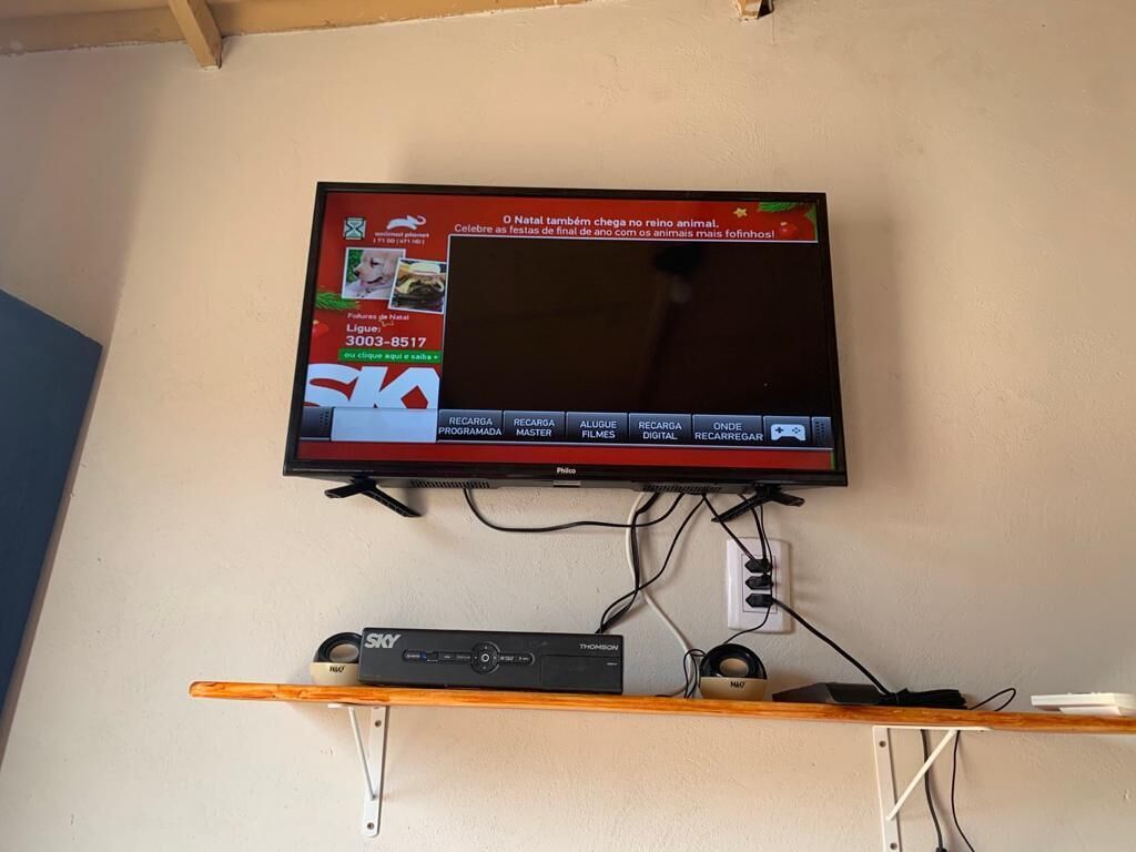 A television mounted on a wall with a remote control and a cable box below it.