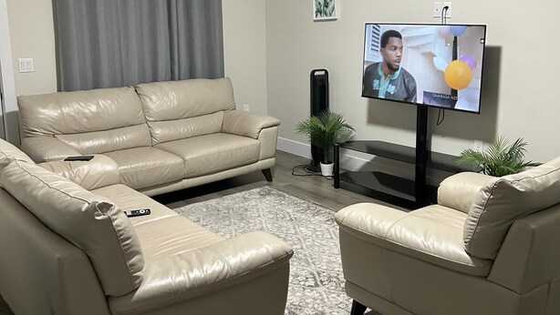 Ein modernes Wohnzimmer mit einem beigefarbenen Ledersofa, einem passenden Sessel, einem Flachbildfernseher und einem kleinen Beistelltisch.