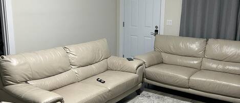 Un salon avec deux canapés en cuir beige, un tapis à motifs et une porte blanche avec un rideau gris.