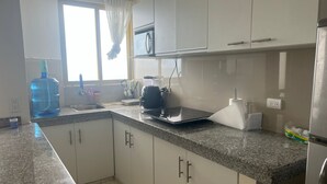 Una cocina moderna con armarios blancos, encimera de granito, dispensador de agua, microondas y tostadora.