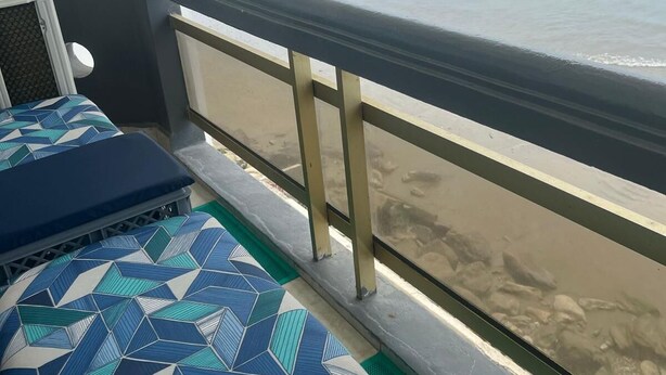 Un balcón con vista a la playa, un cojín estampado y una barandilla.