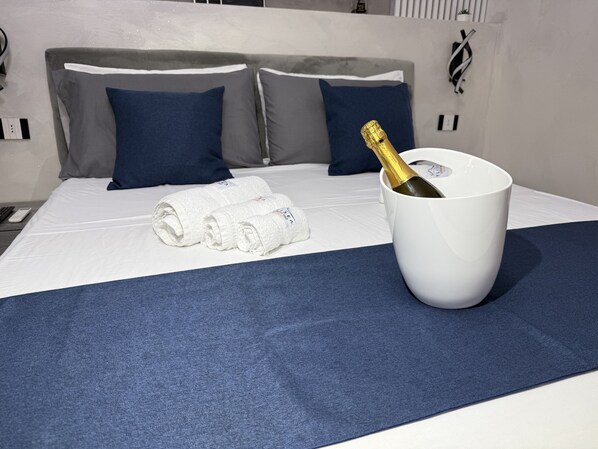 A neatly made bed with a white duvet, two rolled towels, and a white bucket with a champagne bottle. - Ylisea Luxury B&B (Naples)