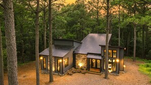 Eine Holzhütte mit Steinunterbau, zwei separaten Zimmern und einem zentralen offenen Bereich mit Sitzgelegenheiten.