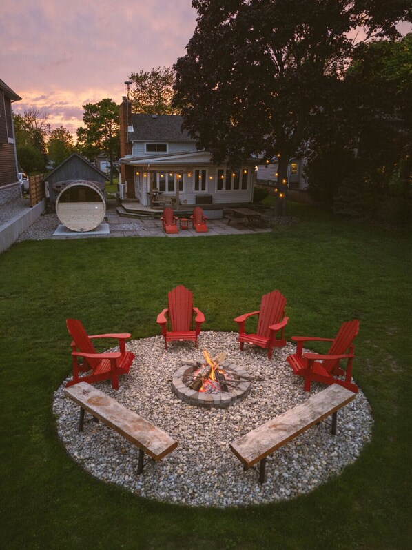 A backyard with a fire pit surrounded by red Adirondack chairs and a wooden bench. - Sauna, stunning views of Lake Erie, lakefront retreat (Kingsville)