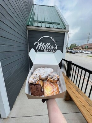 A hand holding a box of assorted pastries in front of a bakery named 'Miller's Bakery'. - Sauna, stunning views of Lake Erie, lakefront retreat (Kingsville)