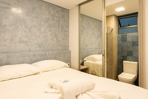 A modern hotel room with a large bed, a glass shower enclosure, and a view of the city. - Beach Class Resort  (Ipojuca)