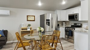 A modern kitchen with white cabinets, stainless steel appliances, and a glass dining table with wicker chairs. - Sweet Suite Retreat,  Studio apartment in Cedar City (Enoch)