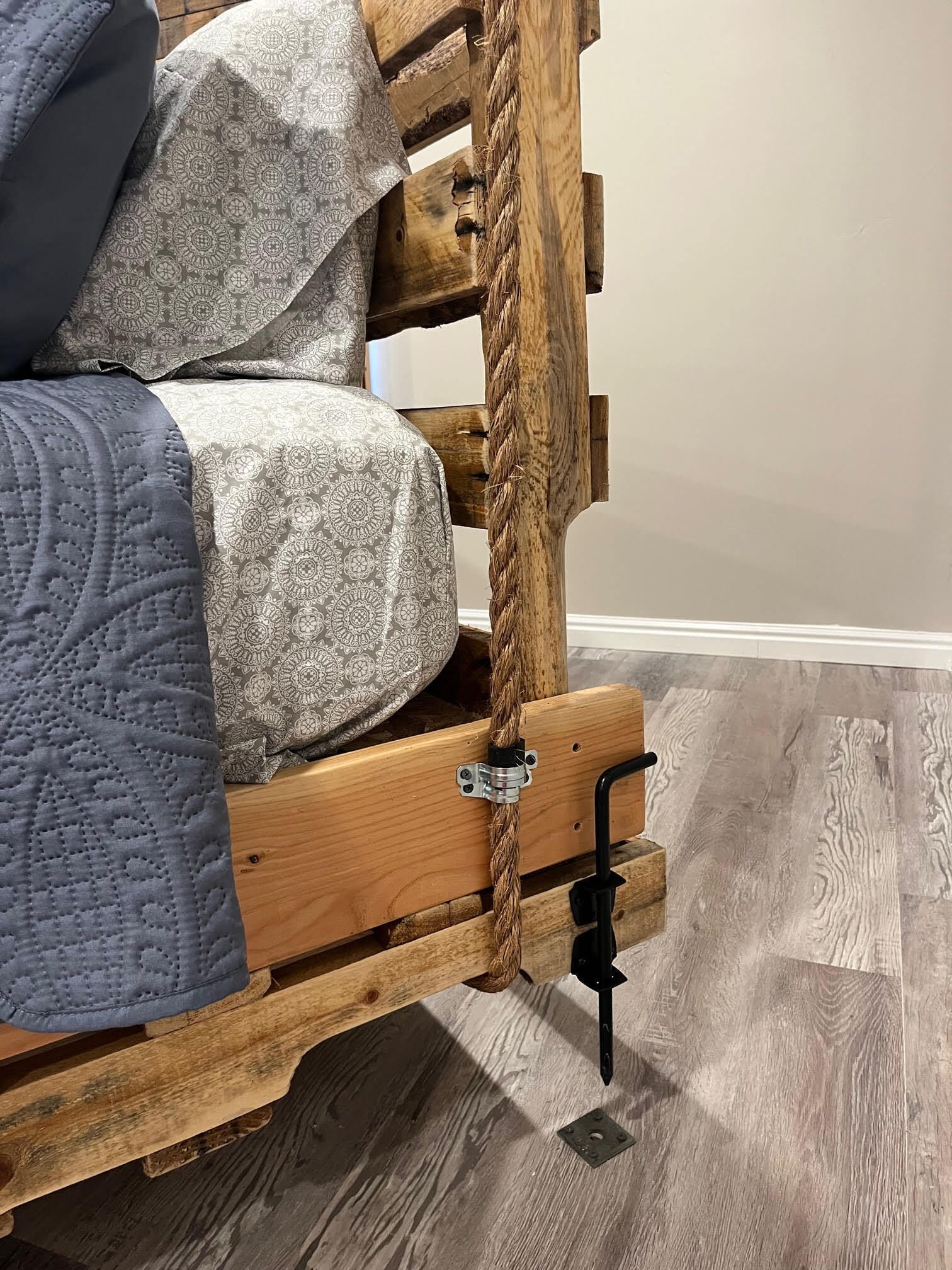 A bed with a wooden frame, a rope, and a metal latch.