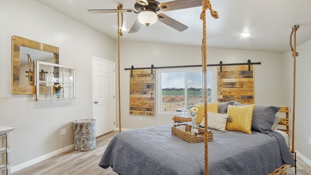 A bedroom with a four-poster bed, a ceiling fan, a large window with a view, and a rustic wooden wall panel. - Sweet Suite Retreat,  Studio apartment in Cedar City (Enoch)