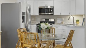 A modern kitchen with white cabinets, stainless steel appliances, a glass dining table, and wicker chairs. - Sweet Suite Retreat,  Studio apartment in Cedar City (Enoch)