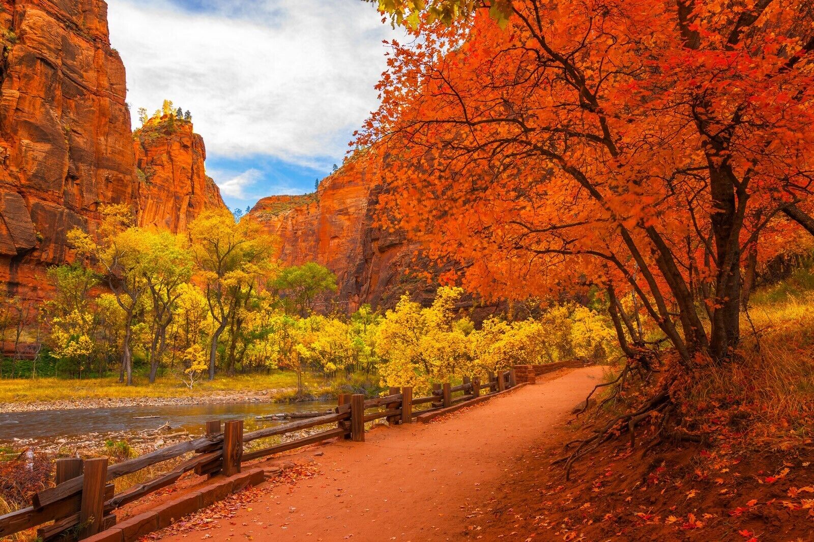 A dirt path flanked by autumn foliage and red rock formations.