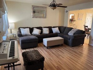Sala de estar com sofá seccional, piano e ventilador de teto.