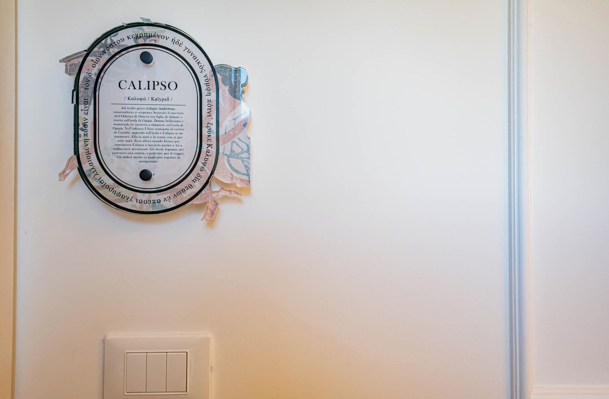 A framed plaque with the name "CALIPSO" and some text, mounted on a wall near a light switch.