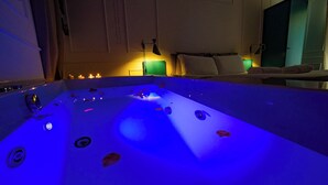 A room with a large bathtub, a bed with pillows, a nightstand with a lamp, and a cabinet. - Giardini Penelope Resort e Spa (Ciampino)