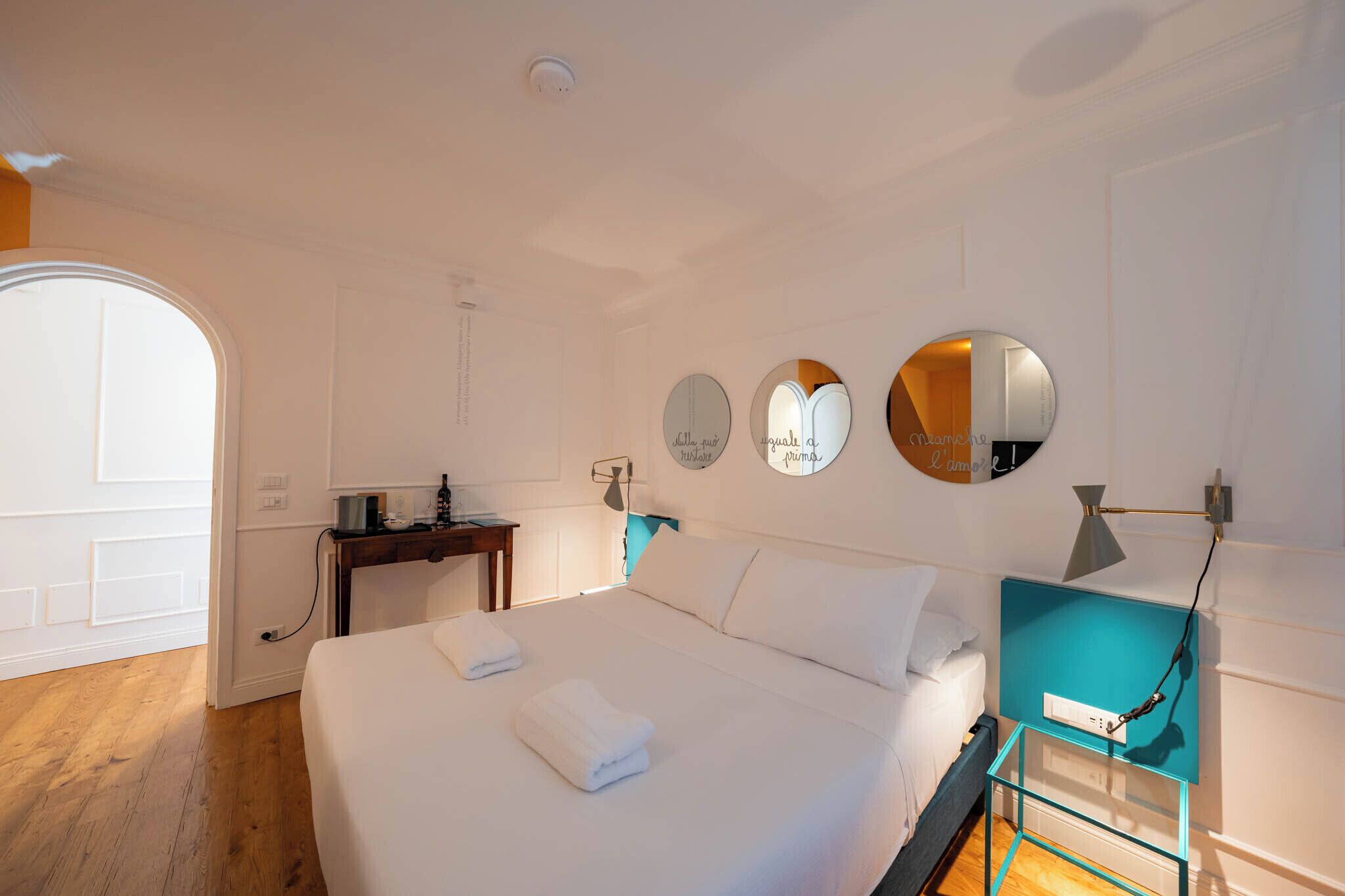A hotel room with a bed, bedside table, and a desk with a chair. There are three round mirrors on the wall.