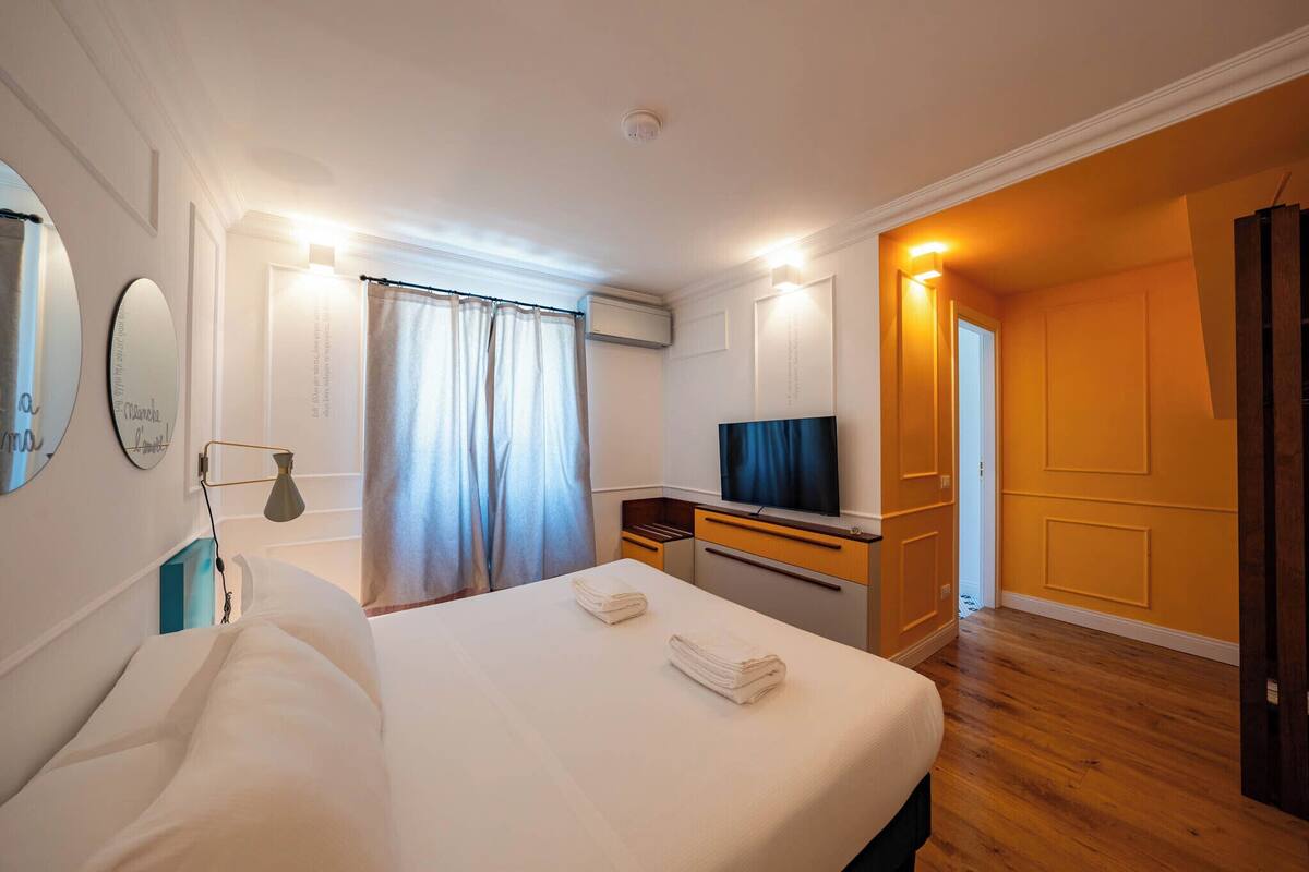 Habitación de hotel con cama, escritorio con televisor, espejo y ventana con cortinas.