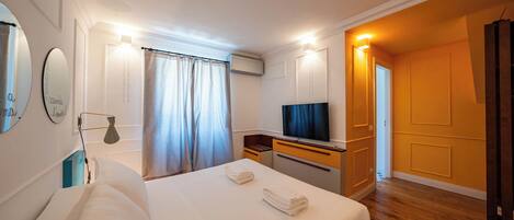 Une chambre d’hôtel avec un lit, un bureau avec une télévision, un miroir et une fenêtre avec des rideaux.