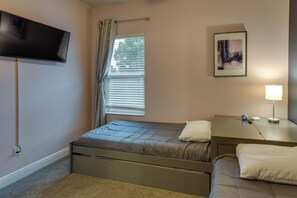 Een slaapkamer met een bed, nachtkastje, lamp, televisie, raam met gordijnen en een schilderij aan de muur.