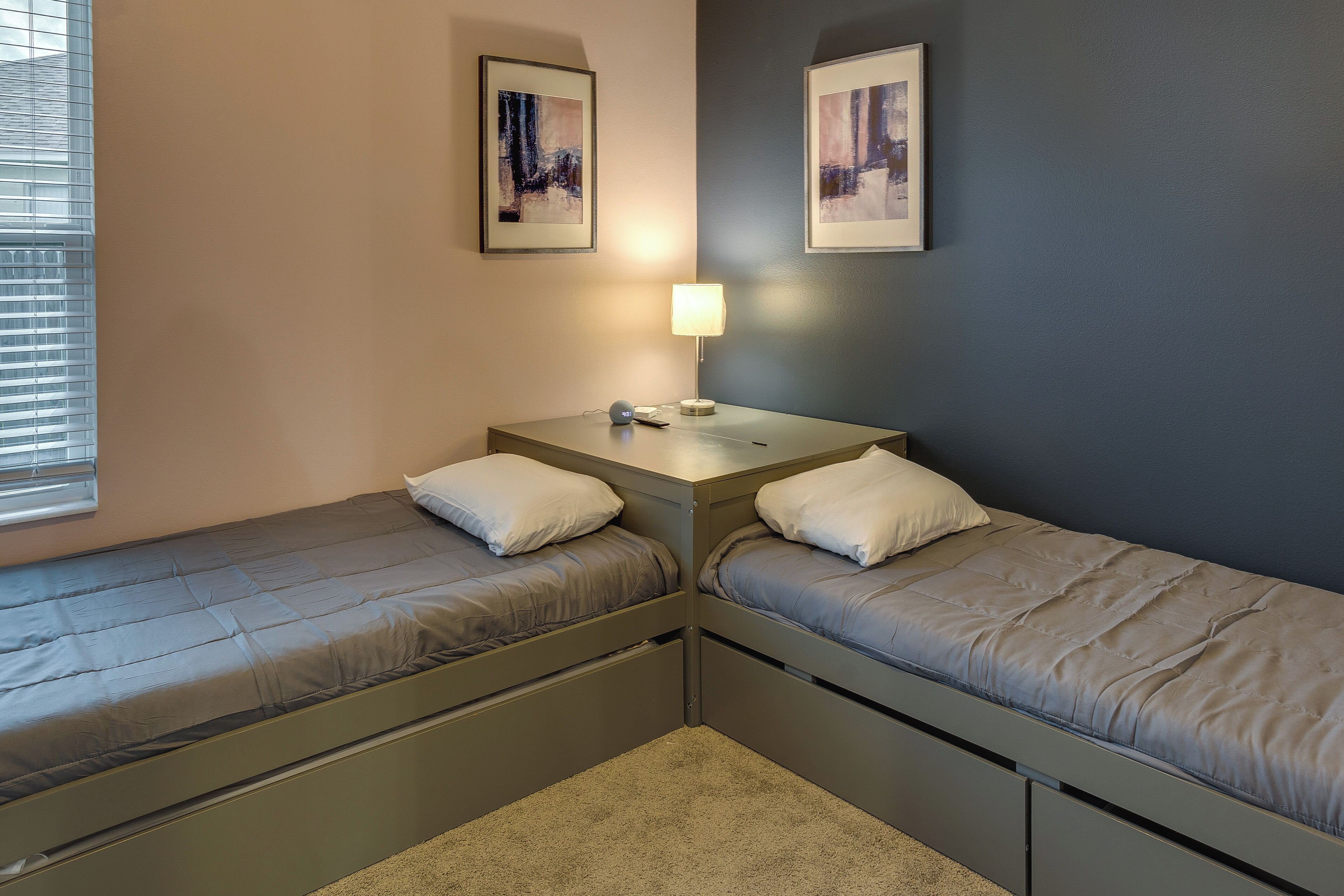 A twin room with two single beds, a small table with a lamp, and two framed pictures on the wall.