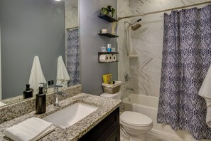 Een badkamer met een wastafel van graniet, een wit toilet en een douche met een decoratieve gordijn.