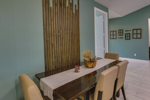 Een eethoek met een houten tafel, beige stoelen, een geweven tafelkleed en een potplant.