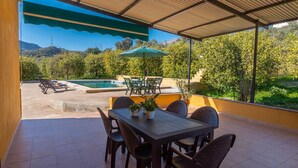Eine überdachte Terrasse mit Pool, Sitzgelegenheit im Freien und Blick auf die umliegende Landschaft.