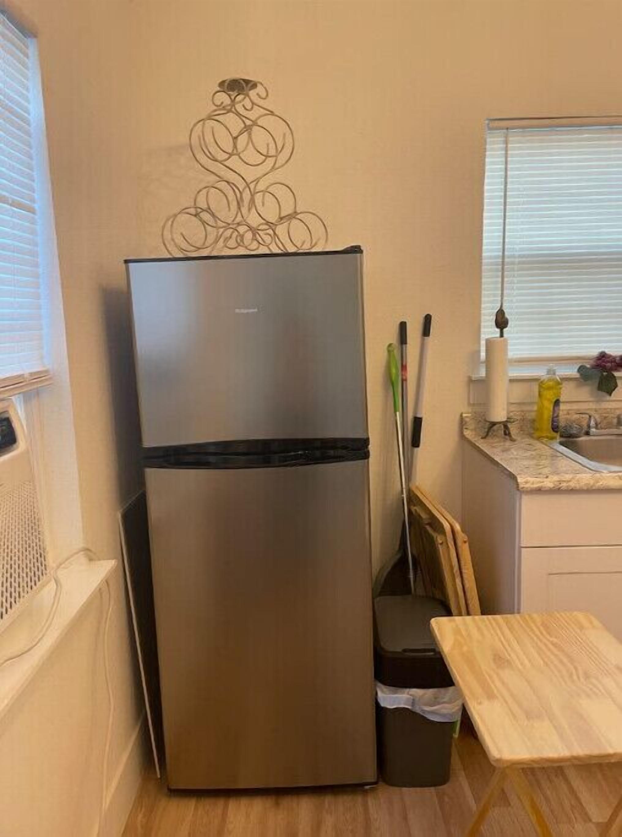 A compact kitchen with a stainless steel refrigerator, a wooden table, and a trash bin.