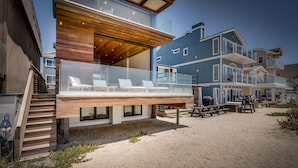 Una moderna casa sulla spiaggia con un balcone in vetro, un pontile di legno e diversi piani.