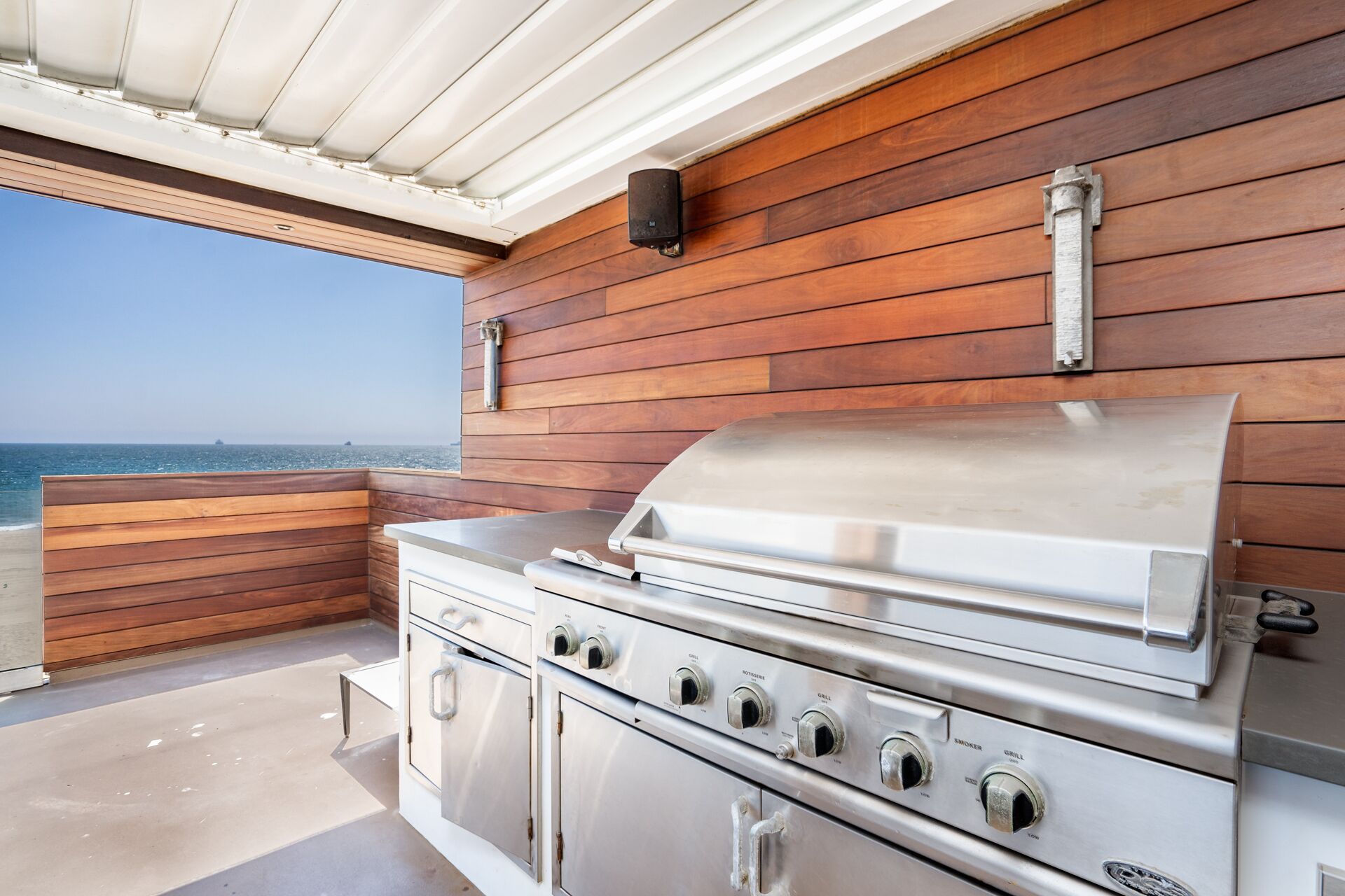 Eine Außenküche mit Edelstahlgrill, Holzwandverkleidung und Blick auf den Ozean.