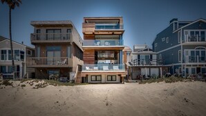 Una casa a più piani direttamente sulla spiaggia, con facciata in legno, ampie vetrate e un balcone.
