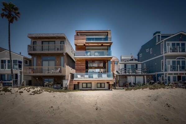 Une maison à plusieurs étages située en bord de mer, avec une façade en bois, de grandes fenêtres en verre et un balcon.