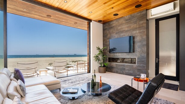 Un soggiorno moderno con un'ampia finestra vista spiaggia, una televisione a schermo piatto montata a parete e un'area salotto confortevole con divano e poltrone.