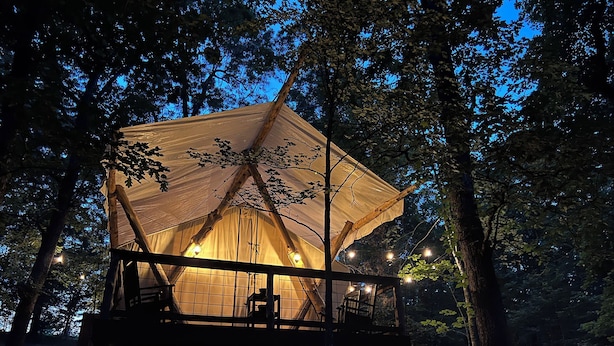 A tented accommodation with a wooden deck and string lights, surrounded by trees.