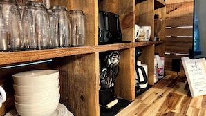 A kitchen area with wooden shelves holding glass jars, a coffee machine, and kitchen utensils.