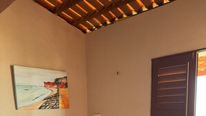 A room with a wooden bench, chairs, a painting of a beach, and a door with shutters. - Chalé panulirus (Icapuí)