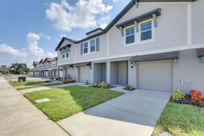 Townhouses with single and double garage doors line a paved driveway, surrounded by well-manicured lawns and flower beds.