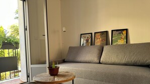 A modern living room with a grey sofa, a small round wooden table with a potted plant, and framed posters on the wall. - Maravilloso Piso a Estrenar en el Corazón de la Ciudad (Vila-real)