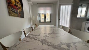 A dining area with a marble table and wooden chairs, a painting on the wall, and a window with a view of buildings. - Maravilloso Piso a Estrenar en el Corazón de la Ciudad (Vila-real)