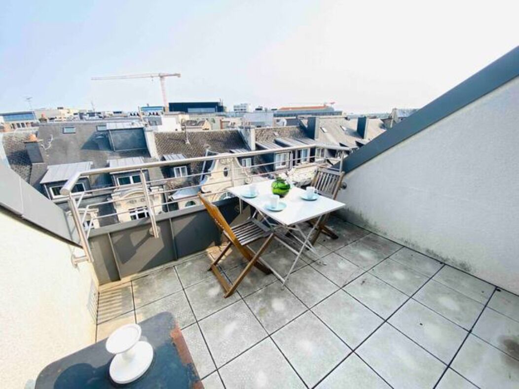 A balcony with a table and chairs, overlooking a cityscape with multiple buildings and a construction crane in the distance.
