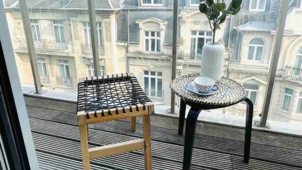A balcony with a small wooden stool and a table with a vase of green plants. - Charming Duplex in Center w. 2 Terraces (Luxembourg City)