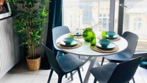 A dining area with a table set for two, a potted plant, and a view of buildings through a large window. - Charming Duplex in Center w. 2 Terraces (Luxembourg City)