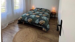 Un dormitorio con una cama, cortinas, una mesita de noche con lámpara y una alfombra tejida.