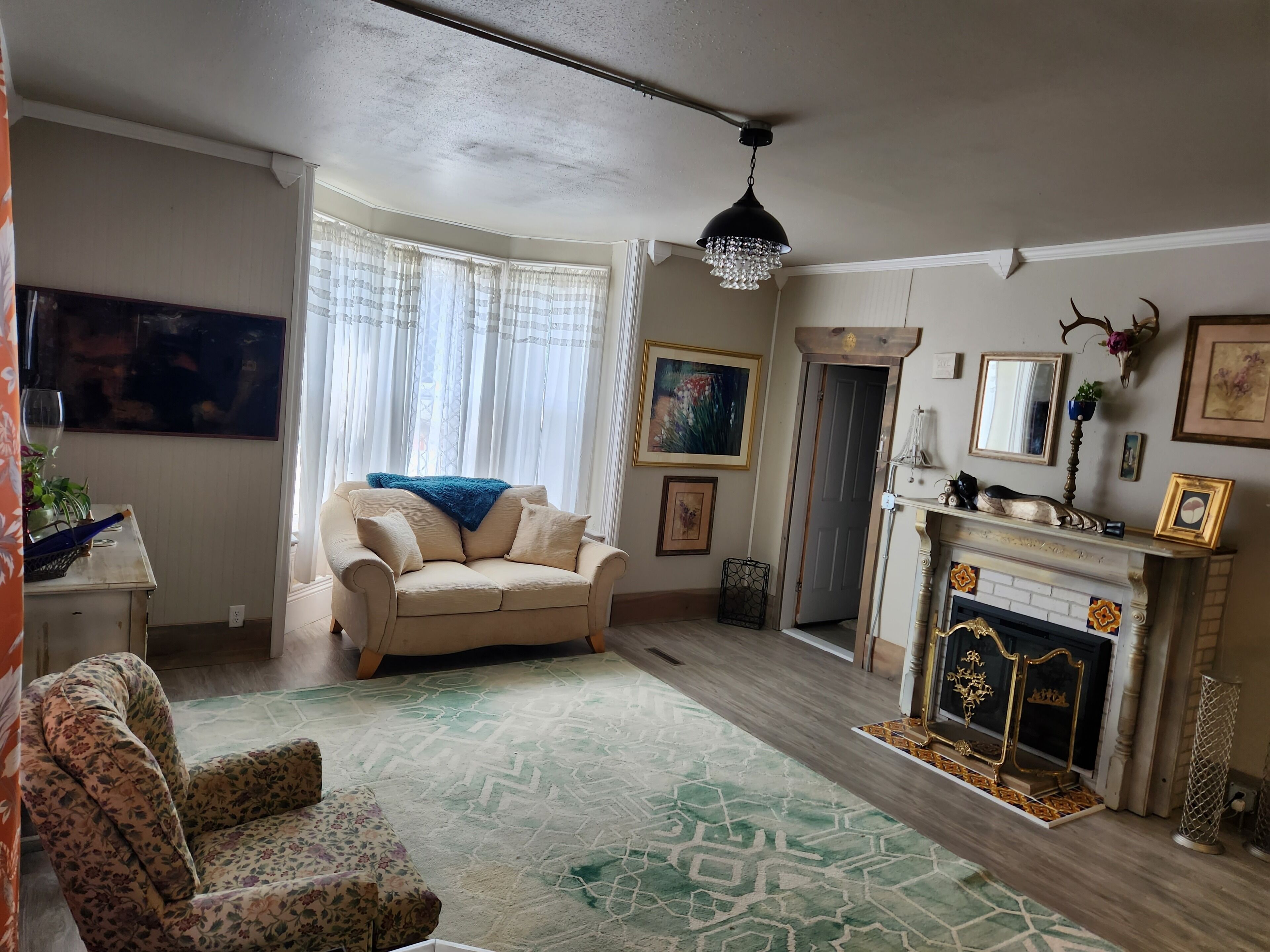 Un salon avec un canapé beige, un fauteuil à motifs, une cheminée agrémentée d’objets décoratifs et un lustre.