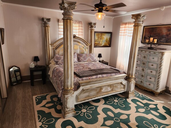 A four-poster bed with ornate columns, a nightstand with a lamp, a dresser with drawers, and a painting on the wall. - Unwind at the Lotus house Opal suite. (Lansing)