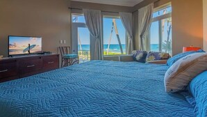 Un dormitorio con una cama grande, un televisor en una cómoda y vistas al océano a través de las ventanas.