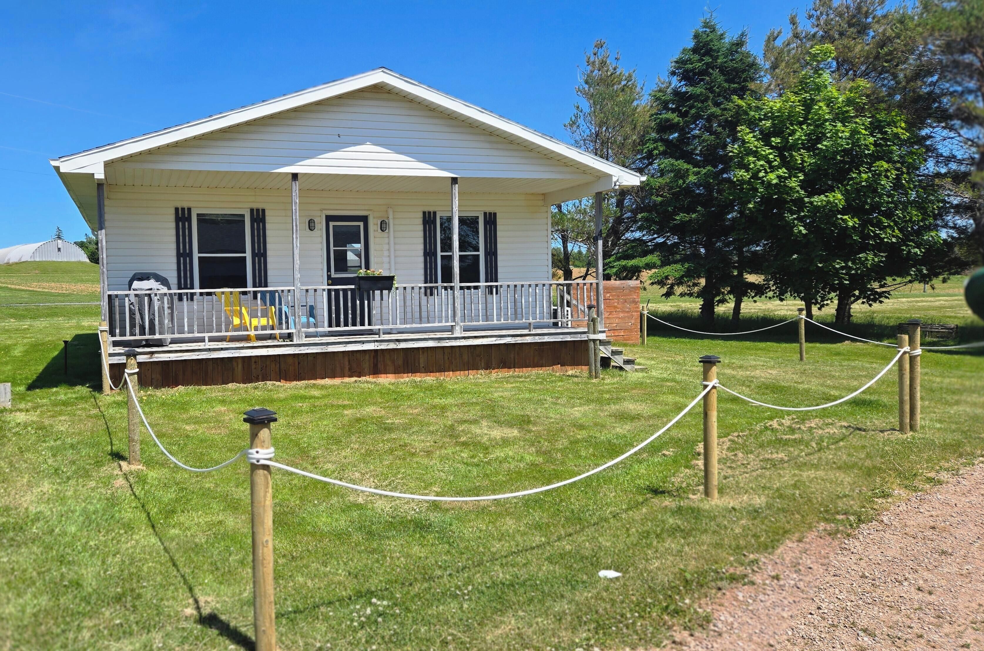 A white single-story house with a porch, surrounded by a chain-link fence and a grassy area.